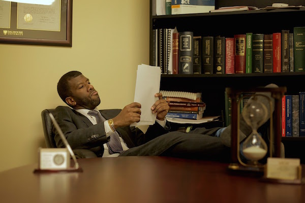 黑人律师莱尔·豪(Lyle Howe)坐在办公桌前的照片。他把脚放在桌子上，正在看一份文件。