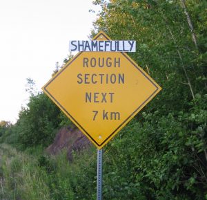 阅读“接下来7公里的粗糙部分”的道路标志有一个手写的标志，说“可耻地”在它上面发布。