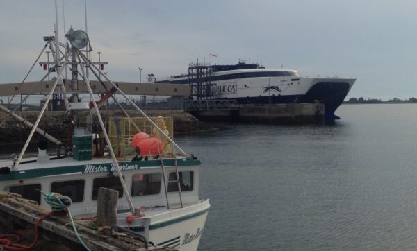 雅茅斯渡船在一个朦胧的夏日靠岸。前景是停靠在码头上的一艘渔船。