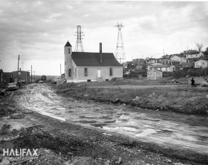 一张泥泞道路旁教堂的黑白照片。背景是房子和电线。