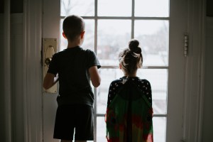 Two children stand at a door looking outside.