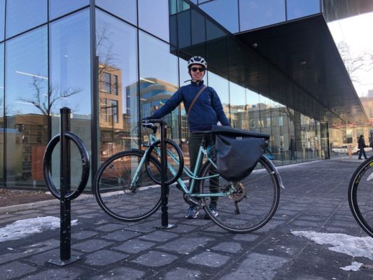 戴着头盔、穿着蓝色风衣的白人妇女吉莉安·班菲尔德(Jillian Banfield)在中央图书馆外骑着自行车