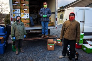 三个蒙面人坐在一辆卡车旁，带着装食物的箱子