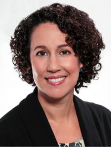 一个微笑的女人的头像，短卷发，穿着黑色西装和印花上衣。