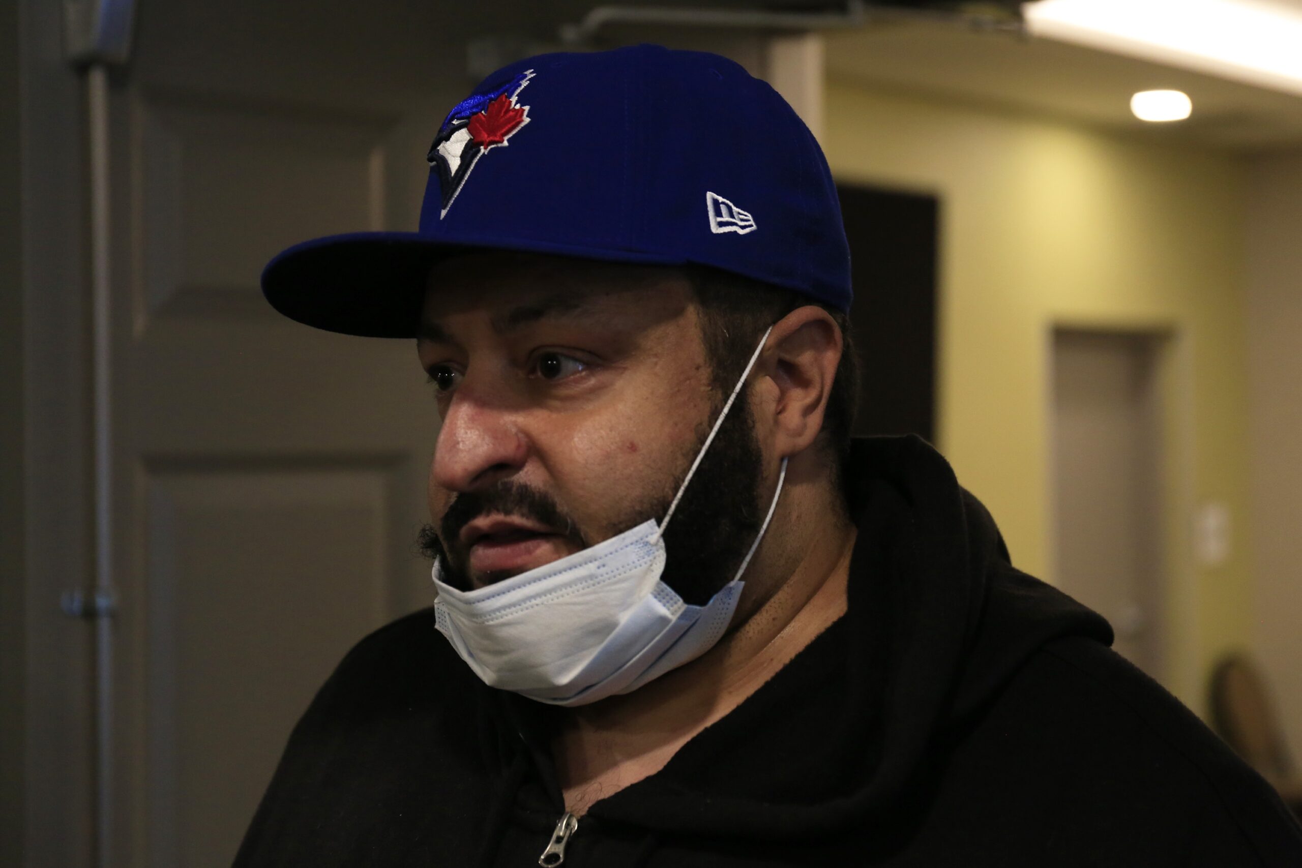 留着胡子的黑色男子戴着蓝鸟帽，下巴上挂着外科口罩。