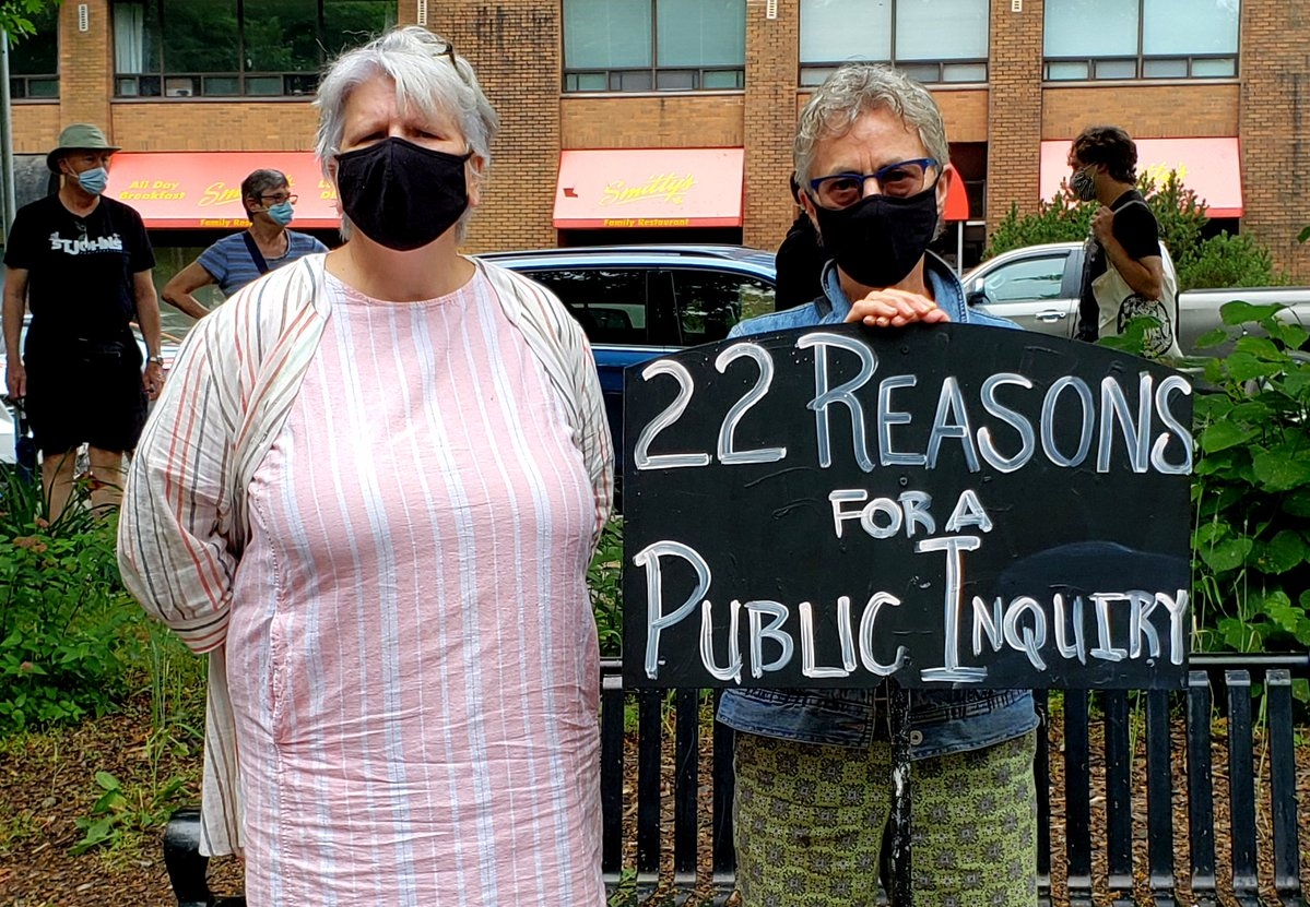 两名妇女戴着黑色口罩，举着一个牌子，上面写着进行公开调查的22个理由