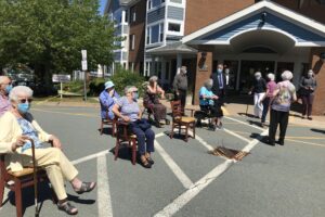 老人坐在养老院停车场的椅子上。