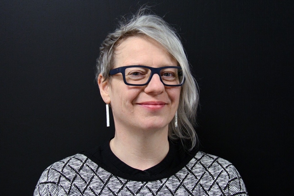 微笑的妇女爆头有银色头发的，玻璃与厚实的框架和被仿造的黑白毛线衣