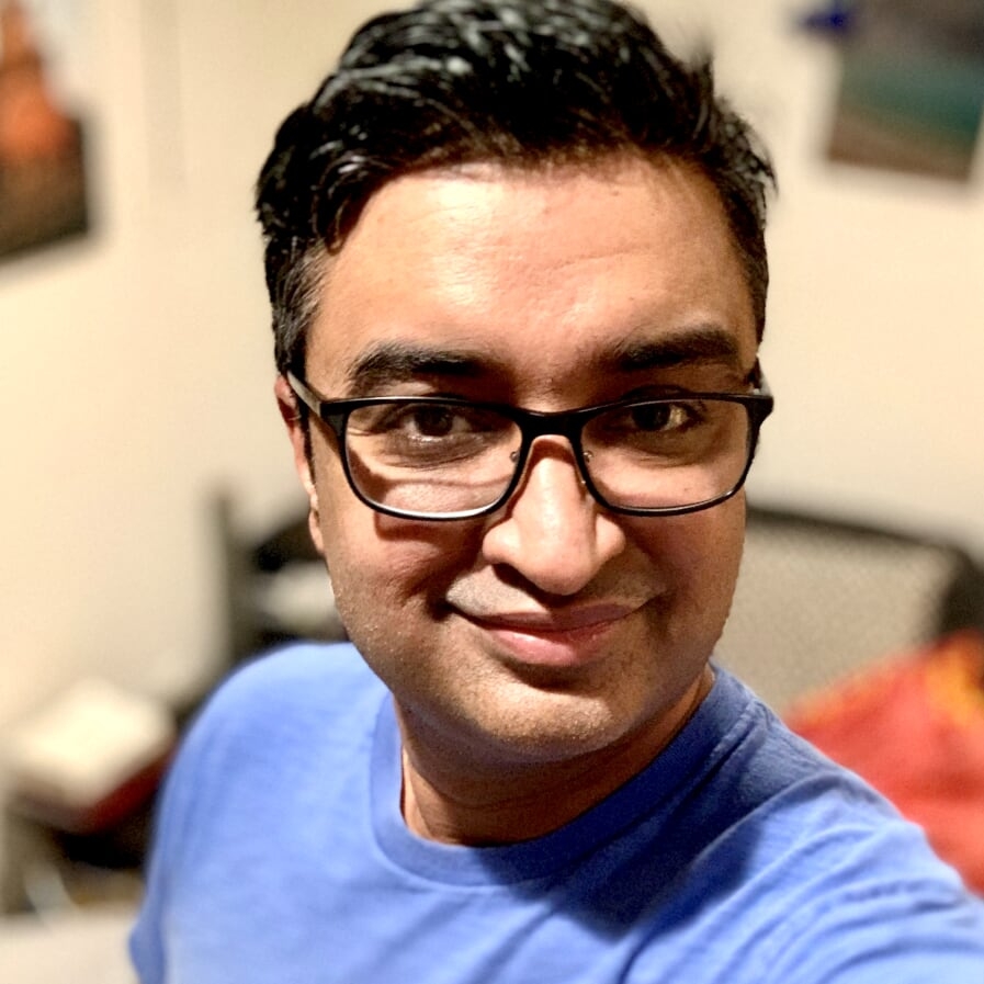 一名南亚男子戴着眼镜，留着黑色短发，看着镜头面带微笑。