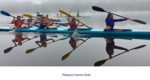 清晨，几艘明亮的蓝色独木舟在平静的水面上滑行。水面上升起了一点薄雾，穿着鲜艳的独木舟运动员和他们的蓝黄色划桨清晰地反射出来。