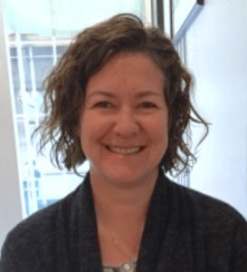 一张丽莎·宾克利的照片，她穿着一件深色毛衣，身后有一扇窗户，对着观众微笑。