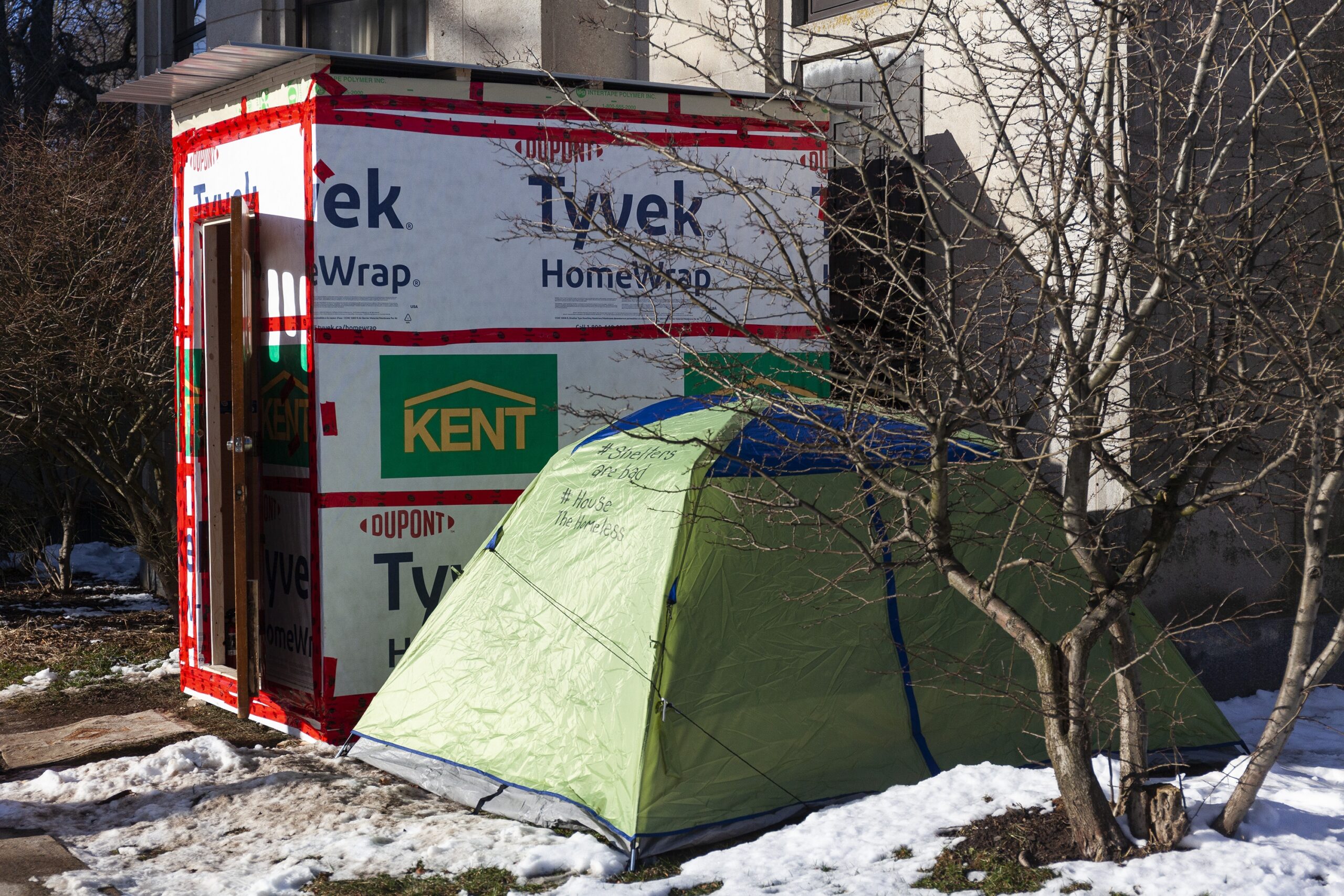 一个绿色的帐篷坐落在雪地上，旁边是一个裹着特卫强的临时避难所。这个庇护所大约有一张双人床那么大，8英尺高，有一扇门。