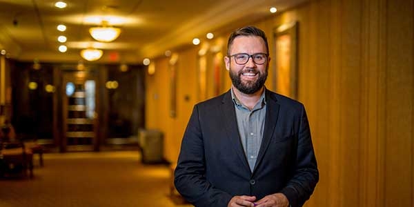 Man in jacket and shirt, in a hallway smiling