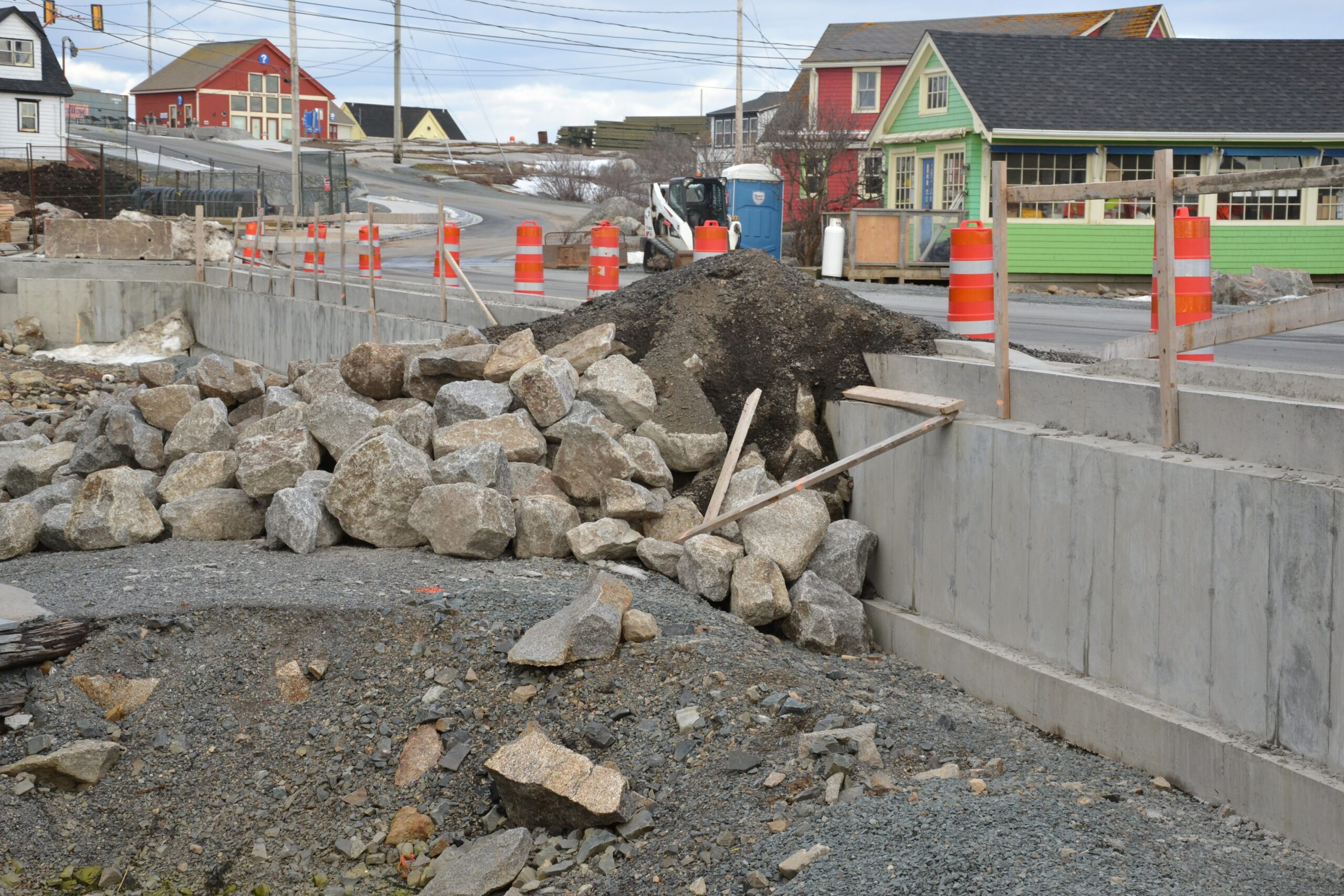 道路建设中有一堆石头和碎石，橙色的圆锥和一个移动厕所作为背景，还有小的，五颜六色的，风景如画的建筑。