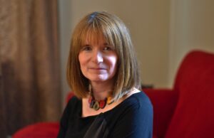 一个深色顶部和充满活力的项链的女人坐在一个红色的椅子上，看着相机，脸上有些严肃。