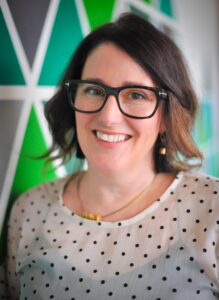 一个妇女的爆头有肩长的棕色头发和玻璃的，在绿色被仿造的背景前面。