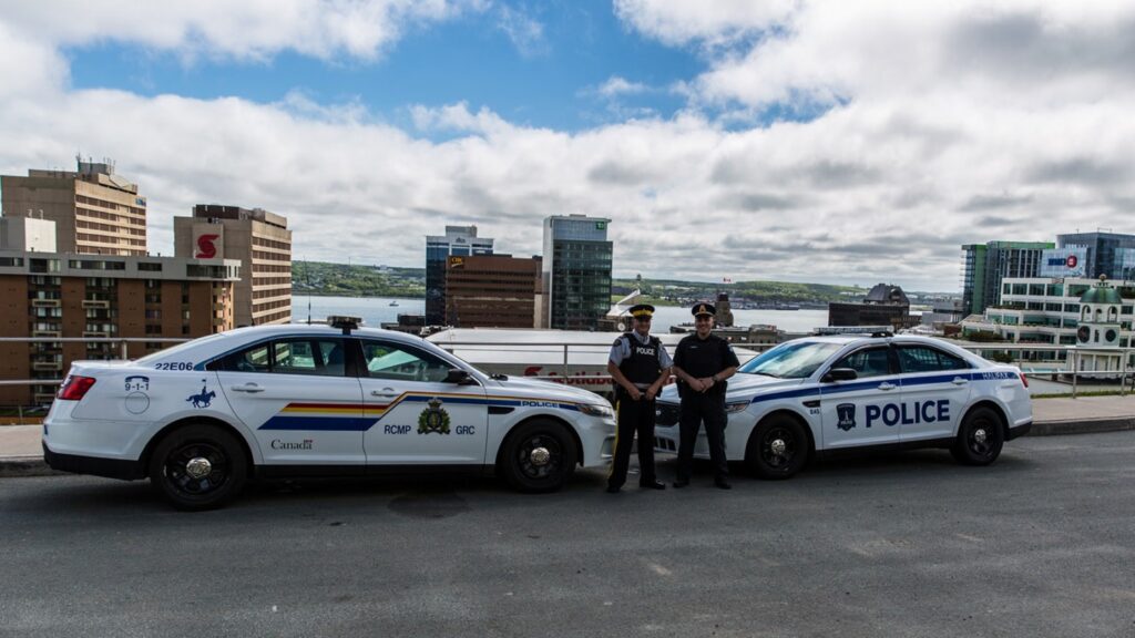 一艘哈利法克斯巡洋舰和一艘皇家骑警巡洋舰停在城堡山。一名警察站在哈利法克斯警车前，一名加拿大皇家骑警站在巡洋舰前。
