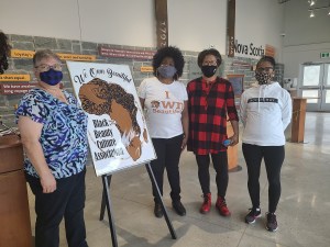 四名戴着面具的妇女站在一个牌子周围，上面写着“我们拥有美丽，黑人美丽文化协会”。
