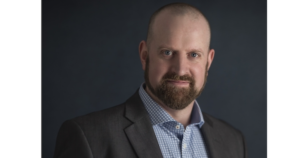 身着西装的保罗·沃兹尼微笑着站在黑暗的背景下。