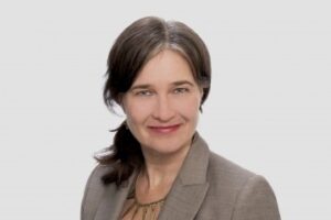 一个妇女的爆头有肩长的头发的在马尾辫，穿着企业夹克和看照相机。