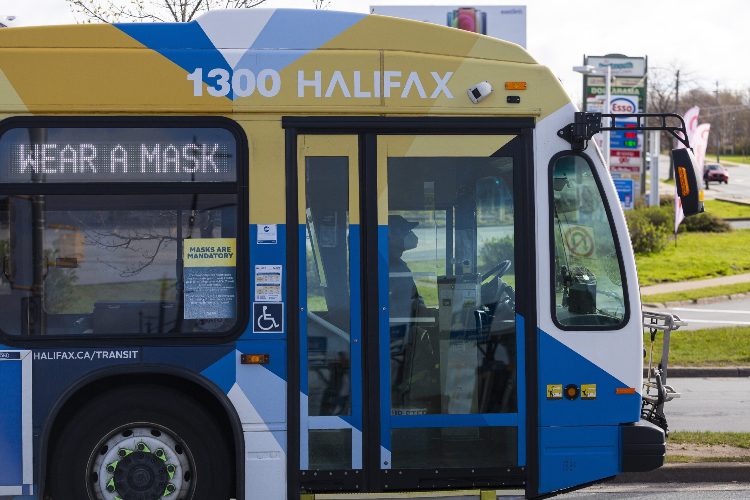 一辆贴着蓝黄白贴花的公交停在停车场。公共汽车上有个牌子写着“戴上口罩”。