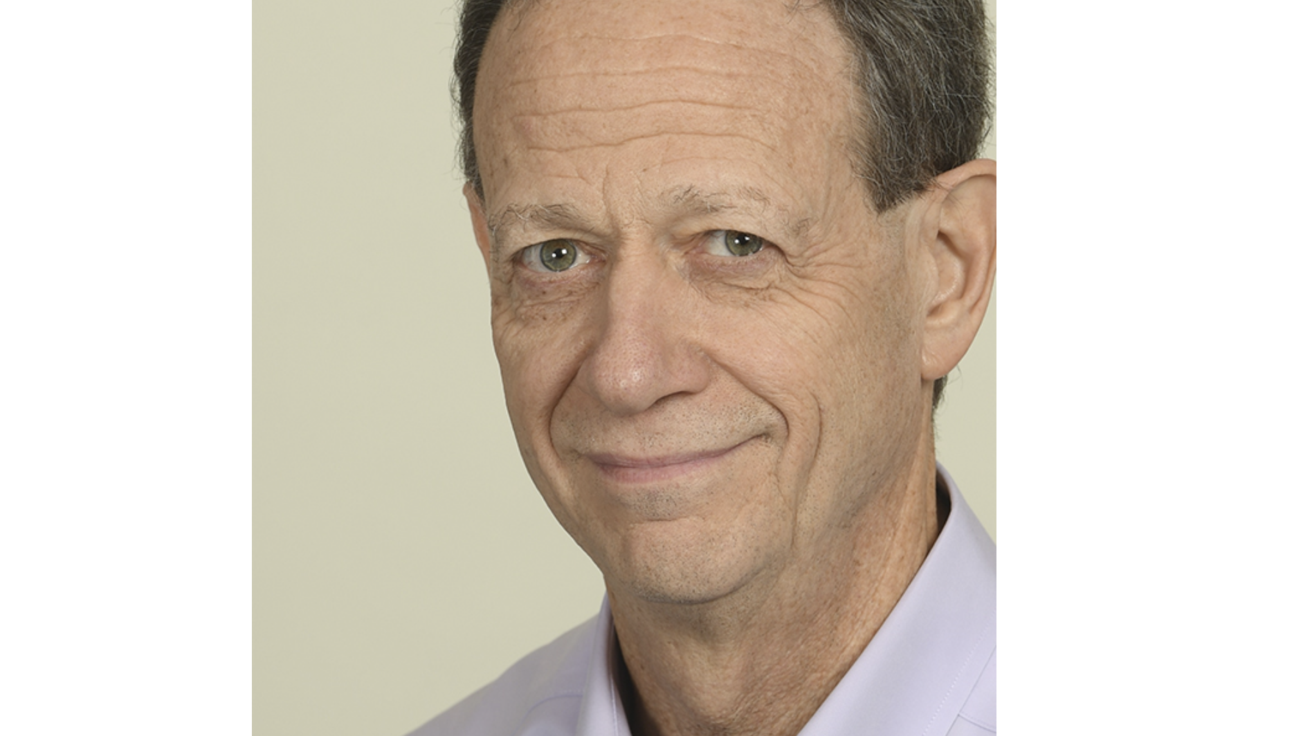 A smiling middle aged man in a pale purple button down shirt smiles at the camera.