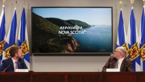 兰金和斯特朗在最近的一次新冠病毒简报会上。他们都面朝前方，但尴尬地转过头去看身后大屏幕上的旅游广告。把你们的椅子转过来，伙计们！