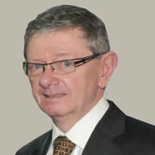 Ralston MacDonnell的照片。他是一个年长的白人男子，穿着深色西装，白衬衫，打着领带。他局促不安地看着镜头，好像他在做什么鬼鬼祟祟的事被抓住了。