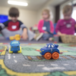 孩子们在印有道路的地毯上玩玩具车。