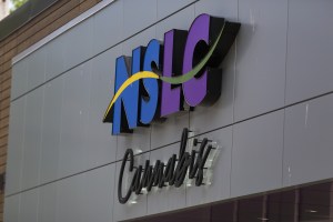 2021年6月，哈利法克斯克莱德街NSLC大麻商店外面的标志。NSLC的标志是蓝色和紫色的大写字母，中间有一个黄色和绿色的波浪。在这之下，大麻是黑色草书文字，从建筑的表面出发。