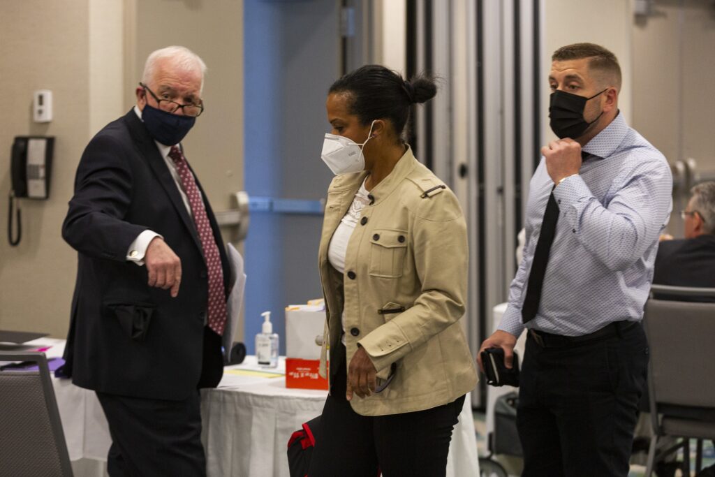 穿着黑暗面具的衣服的一个男人，一名棕色夹克的妇女穿着一件白色面具，和一个男人在衬衫和黑色领带和黑色面具上被看见在会议室。