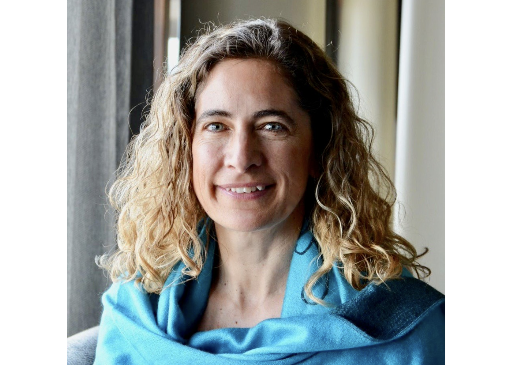 爆头的妇女有肩长的头发的在一件蓝色毛线衣，有窗帘的背景。