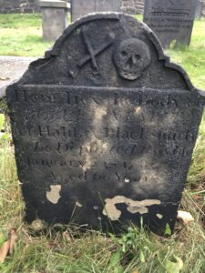 一个非常受风化的墓碑，顶部有一个部分，您可以看到雕刻头骨和一对铁匠的钳子。