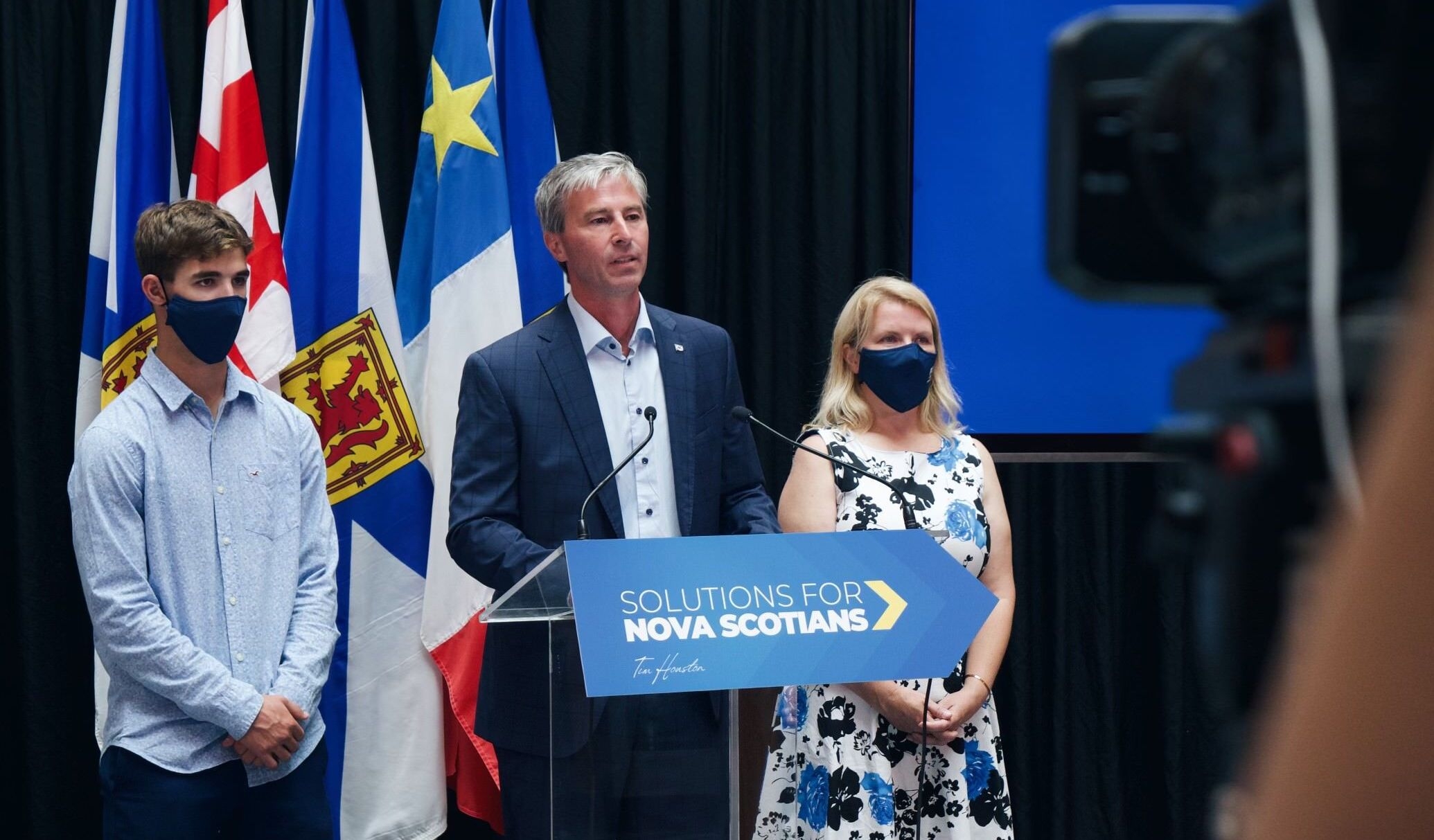 蒂姆·休斯顿站在领奖台上，旁边是他的妻子和儿子。休斯顿没有戴面具，但他的家人戴着。