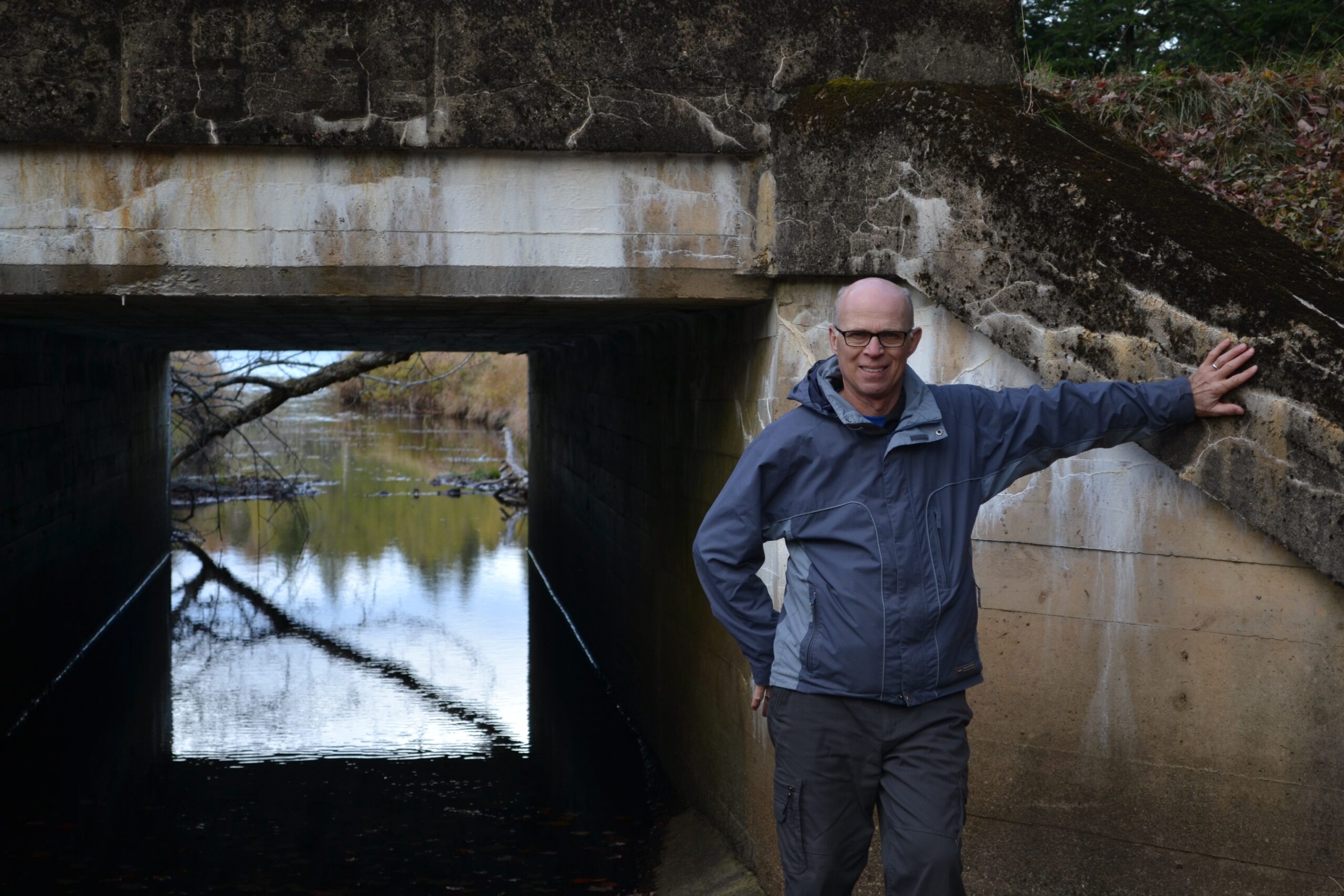 一个穿着雨衣的秃头男人站在混凝土桥台前。