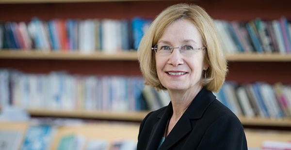 一张中年妇女的大头照，金发短发，坐在书架前。她戴着眼镜，对着镜头微笑。