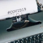 A green typewriter with COVID 19 written in impossibly big type on a sheet of paper on the roller
