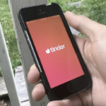 一个男人手里拿着一部手机，手机上的Tinder应用是开着的。
