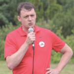 雅各布·基拉维(Jacob Killawee)身穿红色高尔夫球衫，胸前挂着自己的竞选徽章，对着麦克风讲话。