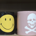 一个笑脸的杯子旁边是一个骷髅头和交叉骨头的杯子。