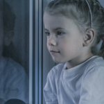 一个小女孩望着窗外，沐浴在傍晚的晨光中