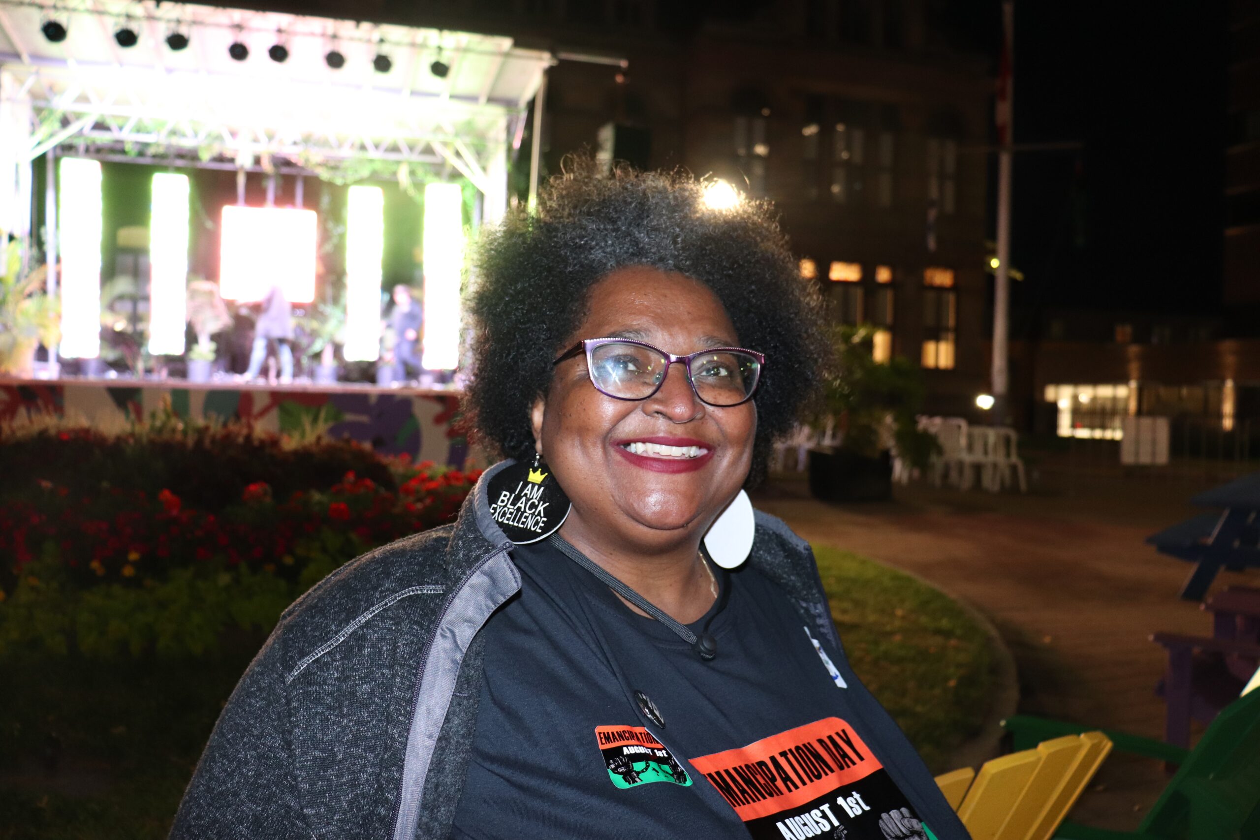 一个微笑的女人戴着眼镜，戴着写着“黑色卓越”的耳环，穿着写着“解放日”的衬衫。