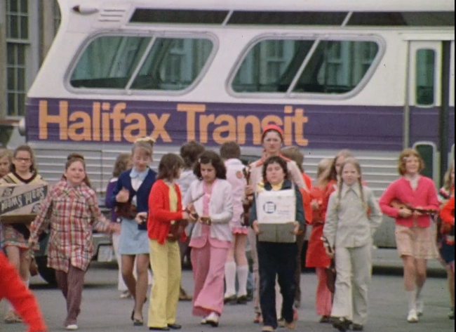 一辆背景上有20世纪70年代哈利法克斯公交公司标志的公交车上，孩子们走向镜头。