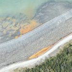 An aerial shot of a bright yellow pool of tailings that appear to be leaking out of a storage pond.
