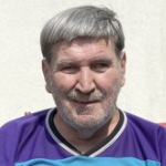 An older man with gray hair and a grizzled chin smiles in the bright sunshine.