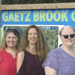 Three women standing in front of the Gaetz Brook Greenway sign.