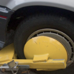 A yellow mechanical boot clamped to a car's wheel