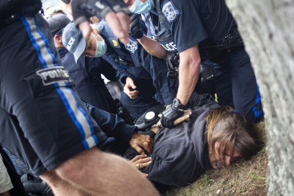 多名警察将一名抗议者按倒在草地上，将他们的手放在背后