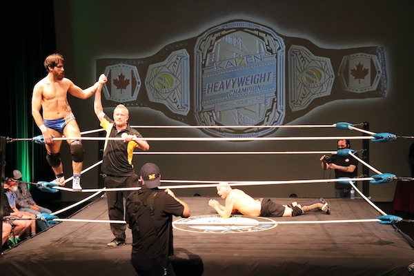 柯维·克里斯特站在绳上，裁判高举着他的手。柯维穿着闪亮的半白半蓝的泳裤，黑色的护膝，白色的摔跤鞋到脚踝以上。裁判穿着黑色裤子和一件黑色短袖领高尔夫球衫，衬衫两侧有黄色镶板。JP·西姆斯躺在拳击场上，难以置信地看着。他光着上身，穿着绿色迷彩镶边的黑色及膝短裤，黑色护膝，还有一双看起来像是长到膝盖的摔跤靴。