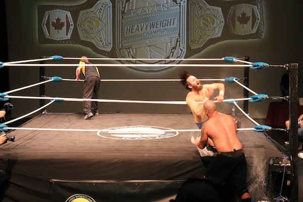 裁判在场地的另一边，背对着他。JP·希姆斯在擂台外，柯维·克里斯特在他的正前方，在他倒下时抓住中间的绳子。